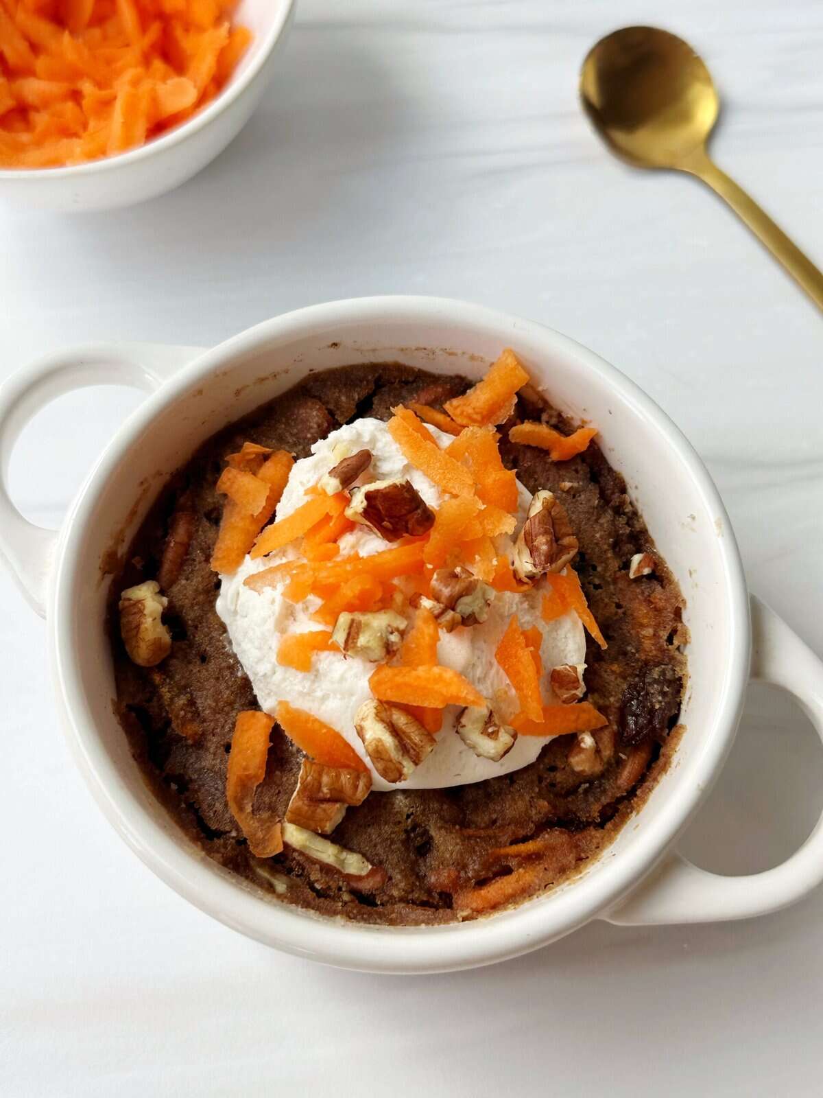 Delicious baked good topped with whipped cream, orange zest, and chopped nuts in a white mug.