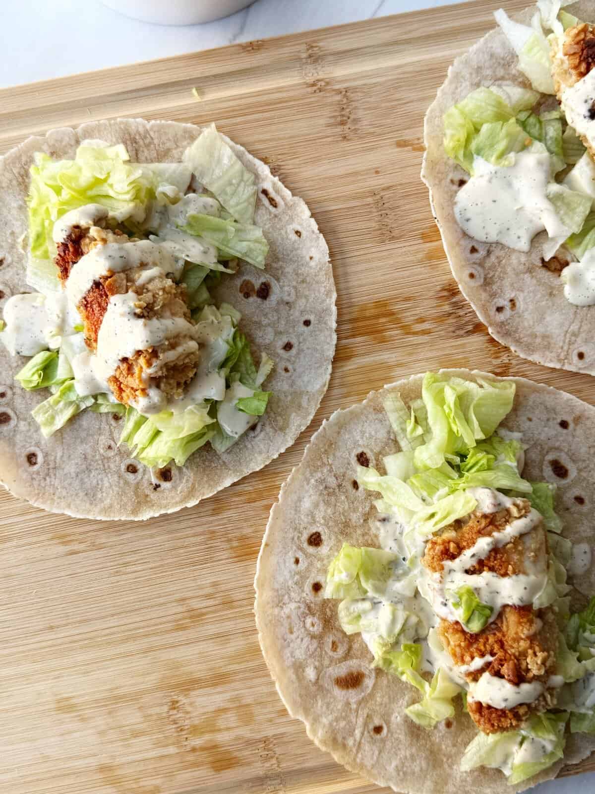 Delicious homemade chicken tacos with lettuce and creamy sauce on a wooden surface.