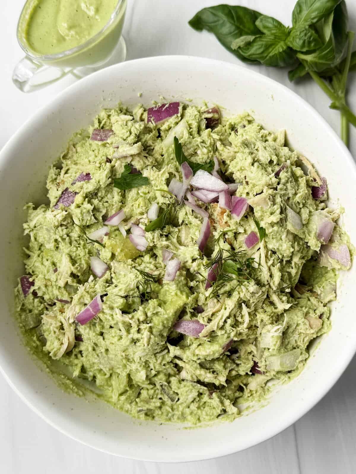 Creamy avocado chicken salad with red onion and herbs in a white bowl.
