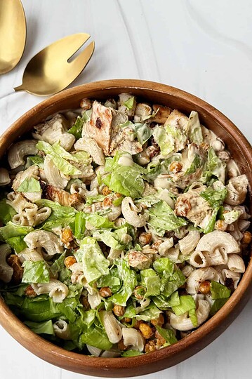 Creamy chicken pasta salad with lettuce, corn, and dressing in a wooden bowl.