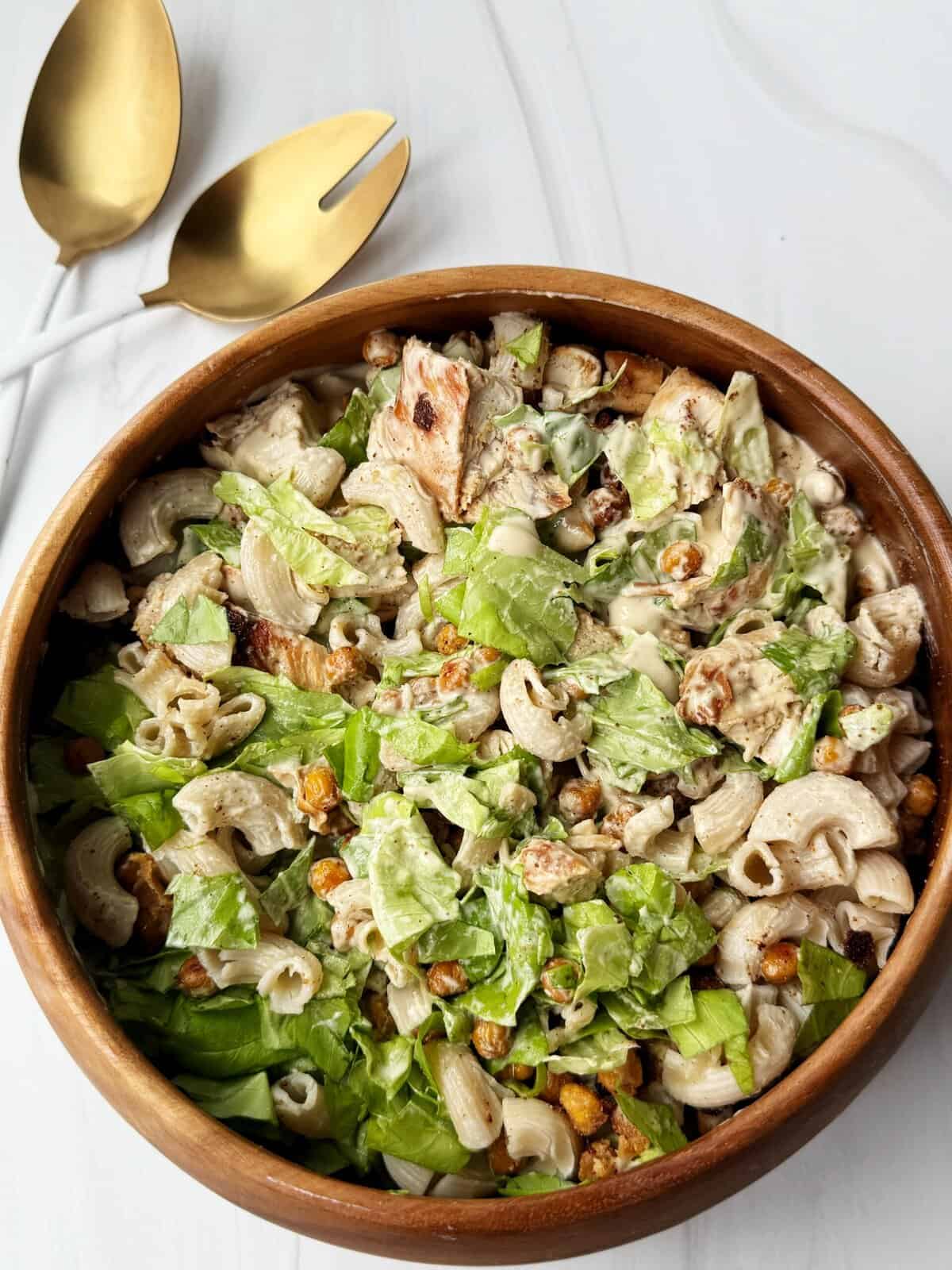 Creamy chicken pasta salad with lettuce and dressing in a wooden bowl.