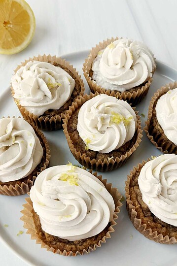 Lemon cupcakes with white frosting on a white plate, fresh lemon half nearby.