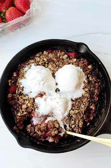Fresh strawberry crumble dessert with vanilla ice cream in a skillet.