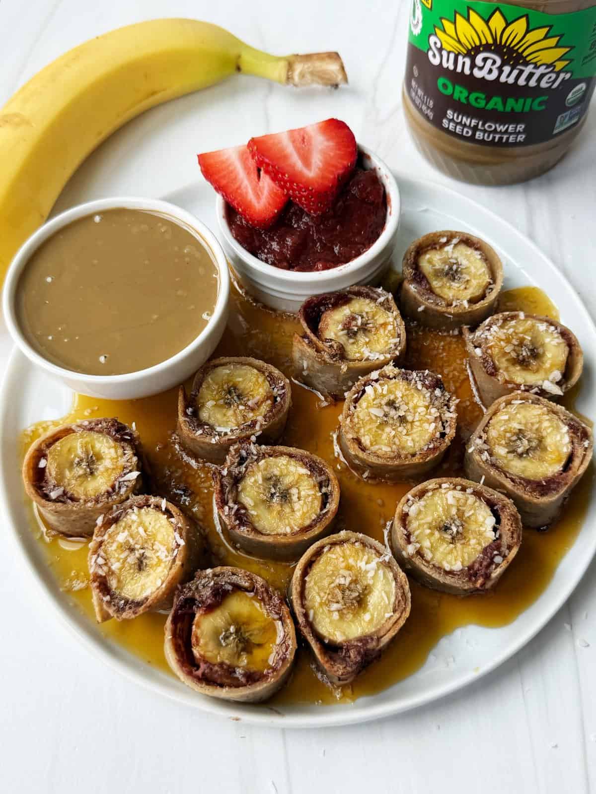 Banana sushi rolls with chocolate, topped with shredded coconut and served with fruit jam and sunflower seed butter