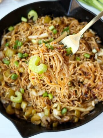 Savory Asian stir-fried noodles with vegetables and green onions in a black skillet.