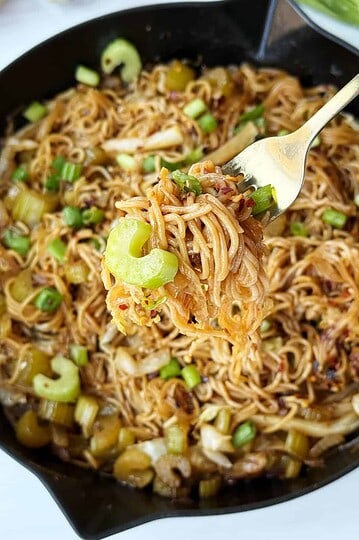Savory Asian stir-fried noodles with vegetables and green onions in a black skillet.