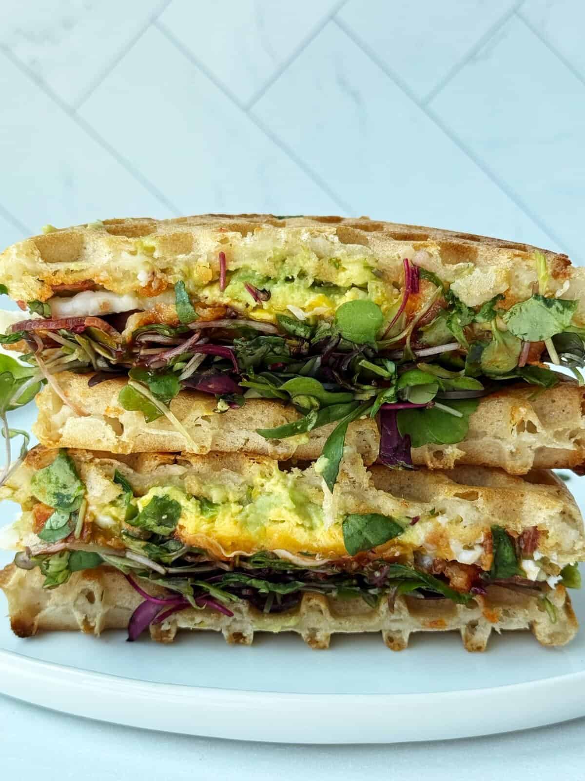 waffle sandwiches stacked on top of each other stuffed with eggs and sprouts