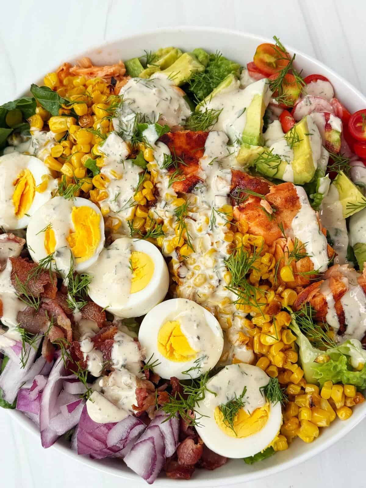 salmon Cobb salad with lettuce, eggs, corn, salmon, red onion and avocado drizzled with ranch