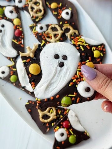 Hand holding Halloween bark with ghost, sprinkles candies and pretzels
