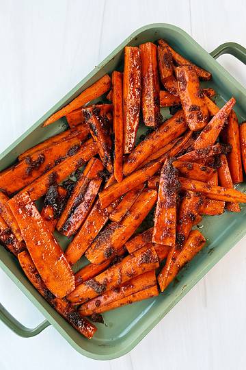 glossy glazed carrots in a green pan