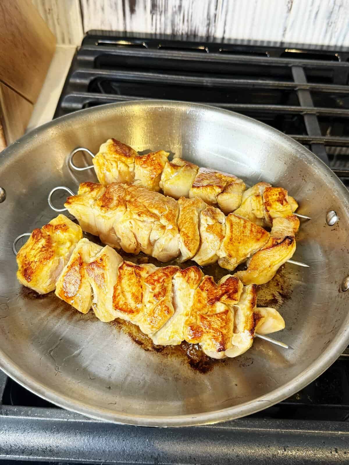 chicken kabobs cooking in stainless steel pan