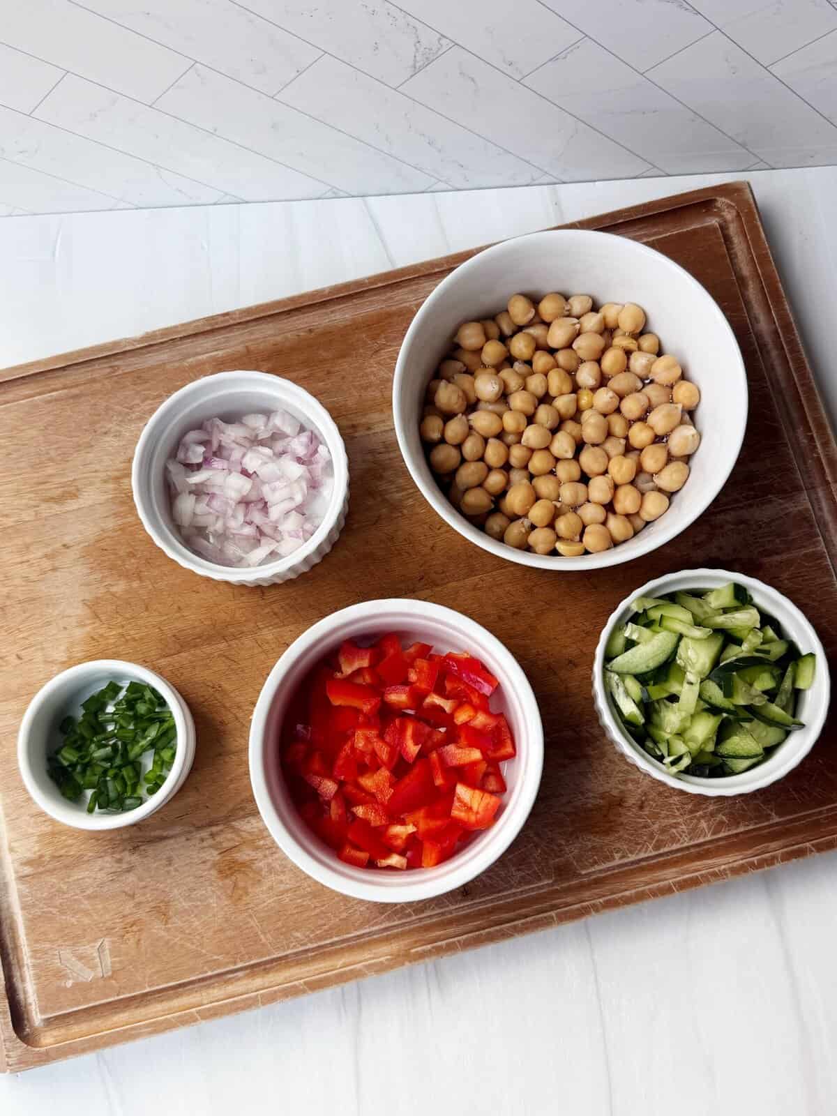 red onion, red pepper, cucumbers, chives and chickpeas on a cutting board