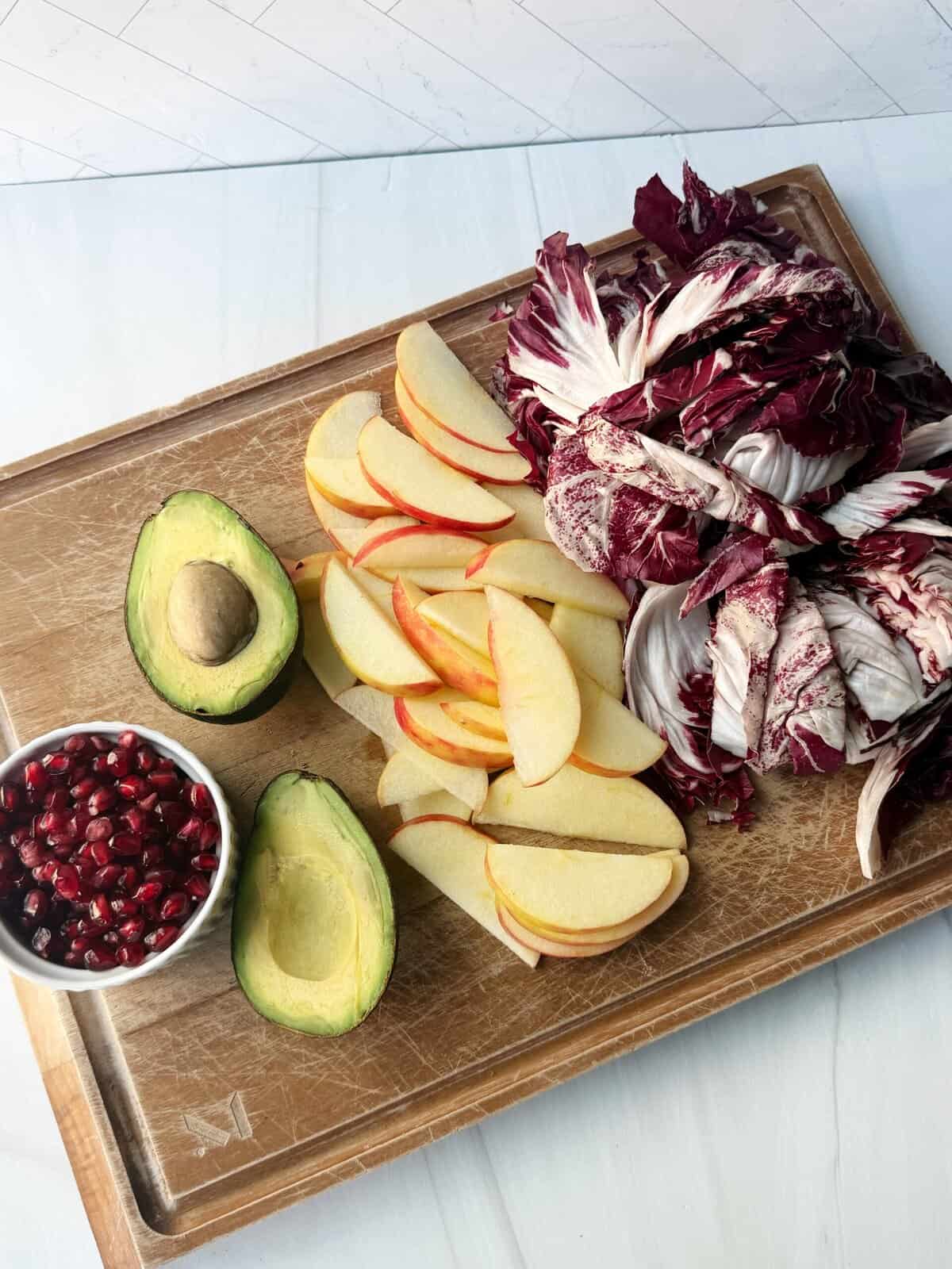 pomegranate seeds, avocado, chopped apple and radicchio on a cutting board
