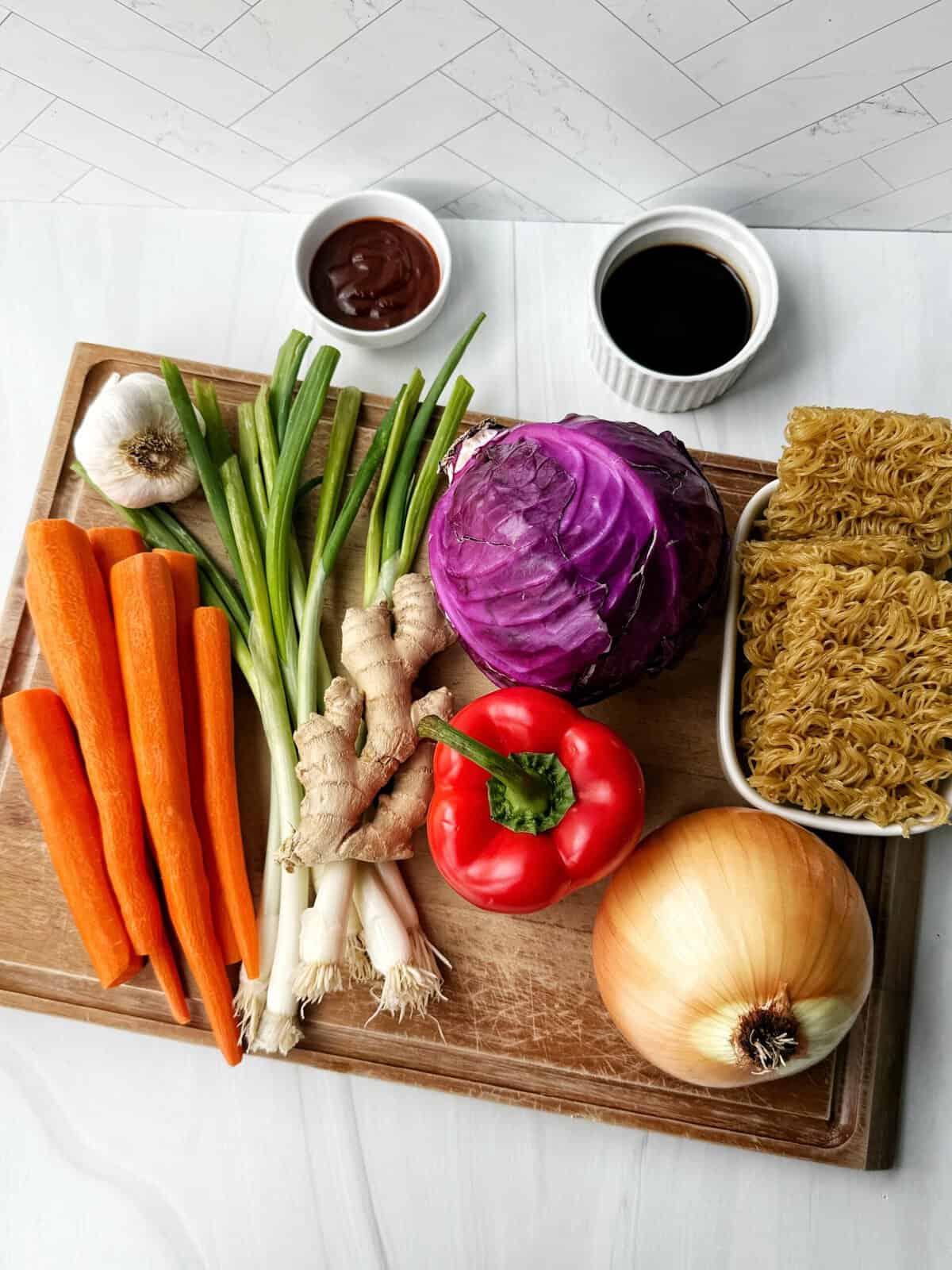 bright colorful vegetables on a wooden cutting board sitting next to ramen noodles