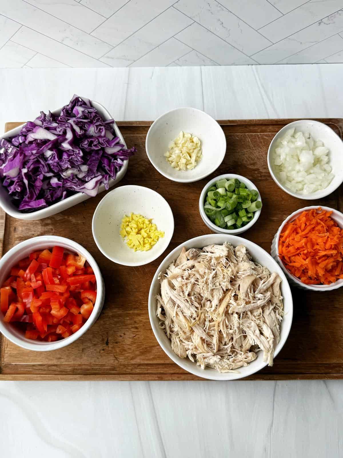 chopped vegetables and shredded chicken on a cutting board