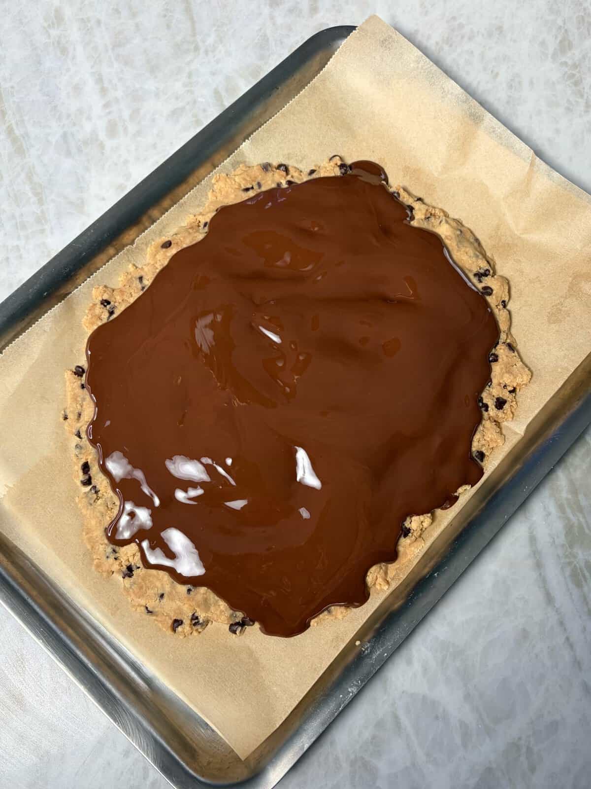 protein cookie dough bark on a baking sheet with melted chocolate on top prote